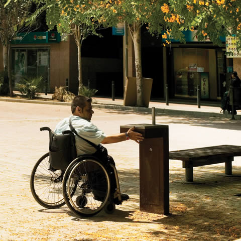Urbidermis Caudal Drinkwater fontein Rolstoelgebruiker drinkt water bij een toegankelijke fontein in een stadscentrum, voorbeeld van inclusieve publieke voorzieningen.