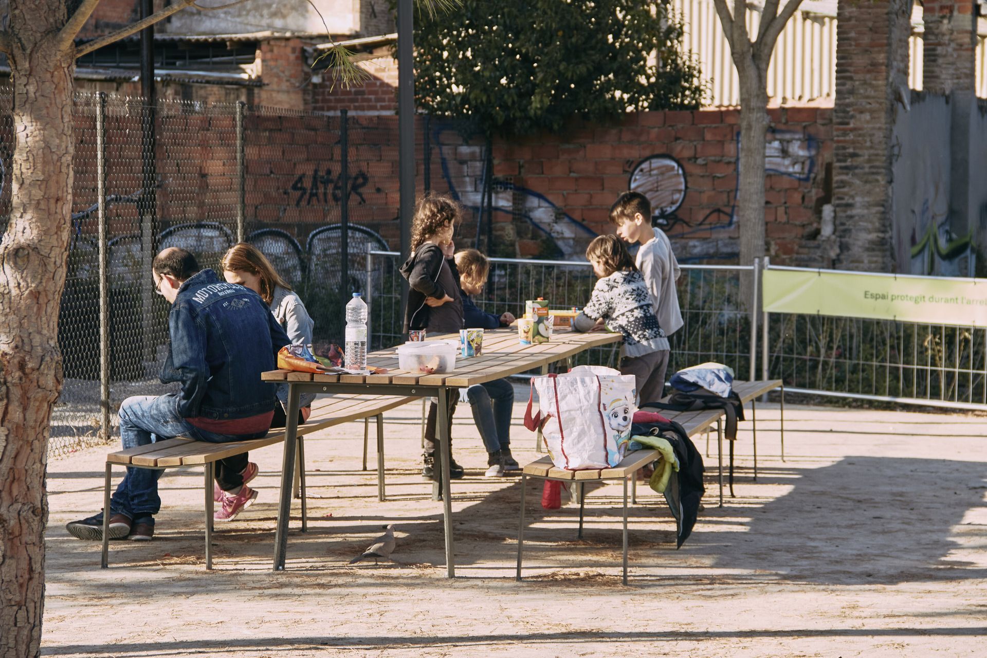 Urbidermis Harpo zitbanken en picknicktafels in een park met een groep mensen. Gezellig en duurzaam straatmeubilair, perfect voor semi-publieke ruimtes zoals schoolcampussen en andere openbare gebieden.