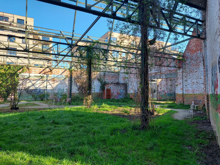 Groene publieke ruimte in Bijgaardepark, Gent, met bewaarde bakstenen muren, stalen draagstructuur, Servibo zitbanken en klimplanten, in contrast met moderne appartementsgebouwen.