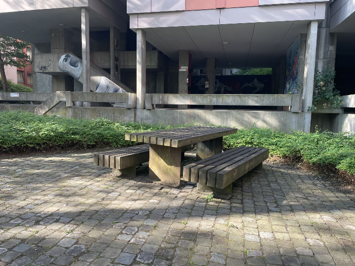 Houten picknicktafel in een stedelijke binnentuin van Camilo Torres, met betonnen gevel en street art, toont hoe sociaal meubilair functioneert in een sobere architecturale omgeving.