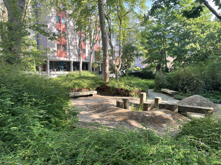 Overzicht van de centrale tuinzone van Camilo Torres met circulaire zitstructuur, robuuste houten banken en omringend groen in een schaduwrijke setting.