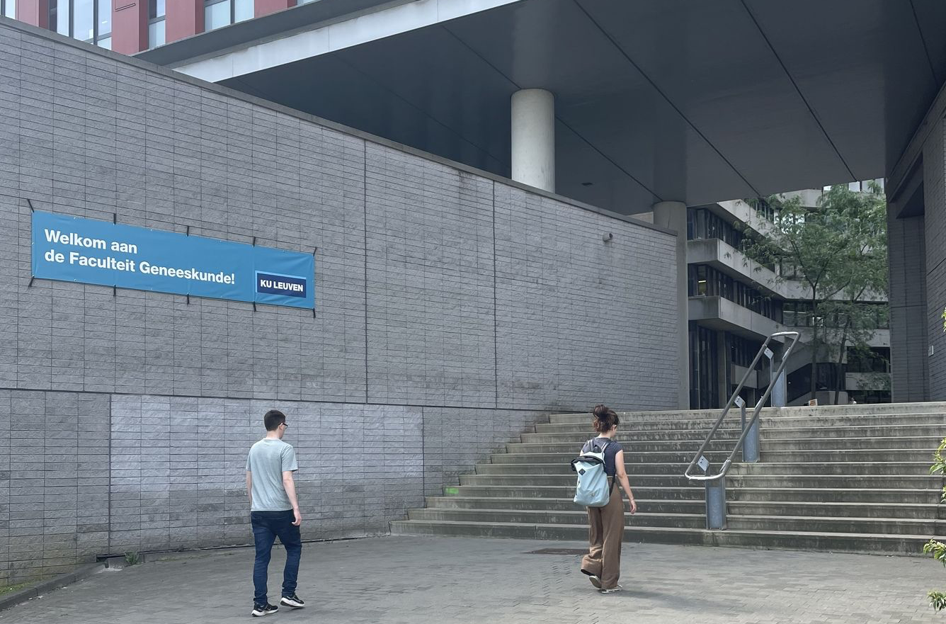 Twee studenten lopen richting een brede betonnen trap aan de Faculteit Geneeskunde op Campus Gasthuisberg van KU Leuven.