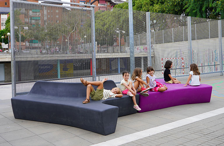 De Twig Air zitbanken van Escofet in zwart en paars in een schoolpleinsetting, uitnodigend voor spel en ontspanning in de stedelijke buitenruimte.