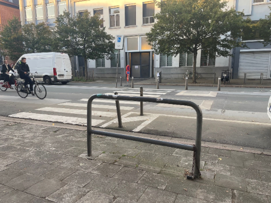 Zebrapad met metalen hek en paaltjes op de stoep die de looplijn van voetgangers naar de oversteek blokkeren.