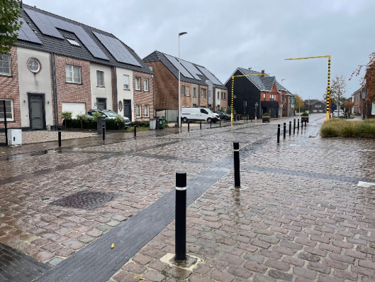 Nieuwe woonstraat met kasseien en een rij slanke zwarte paaltjes langs een donkere strook in het wegprofiel.