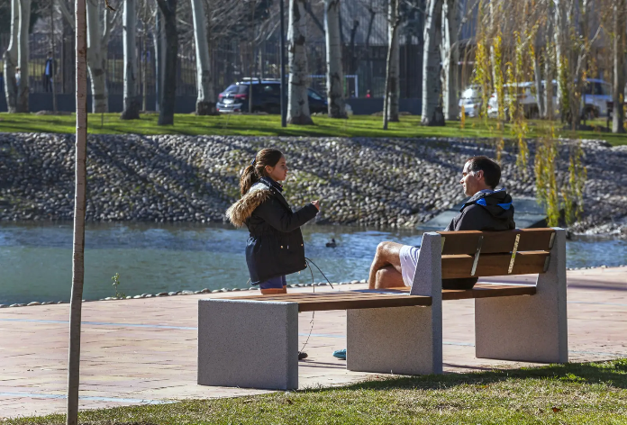 Alpine zitbank aan waterkant in stedelijke groenzone, betonnen steunen en houten latten als rust- en ontmoetingsplek langs promenade