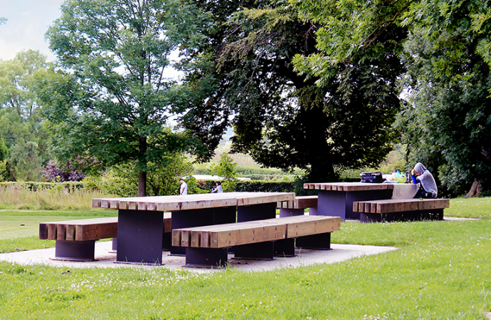 Tramet zitbanken en tafels van Escofet 1886 in hout en staal, opgesteld als robuuste picknickcombinatie zonder rugleuningen en armleuningen in een groene parkzone.