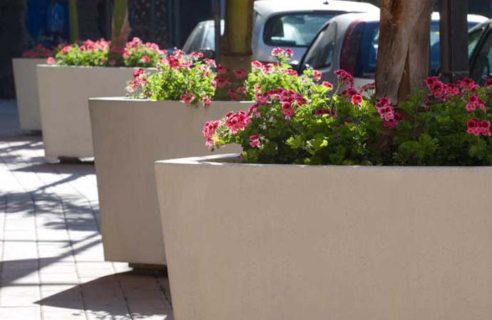 Bilbao plantenbakken van Escofet 1886 in licht gewapend beton, gevuld met roze bloemen en bomen, geplaatst in een stedelijke straatomgeving als groene en decoratieve afbakening van de publieke ruimte.